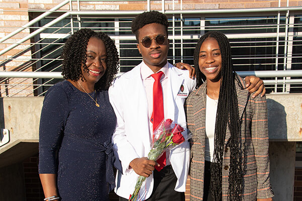 Student holding a rose and wearing their white coat with their family after white coat ceremony