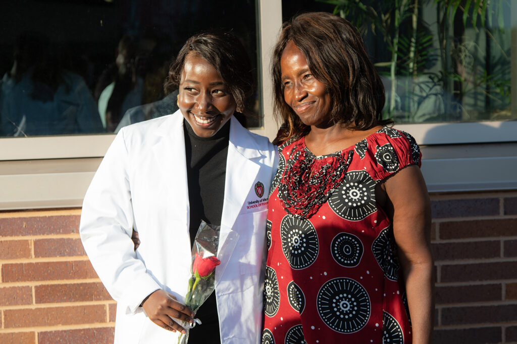 Student holding a rose and wearing their white coat with their mother after white coat ceremony