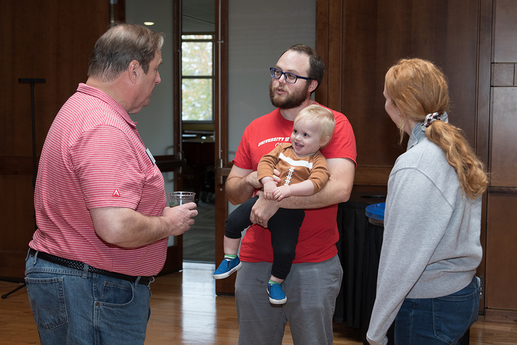 Alumni holding young child talking with Dean Steve Swanson and another