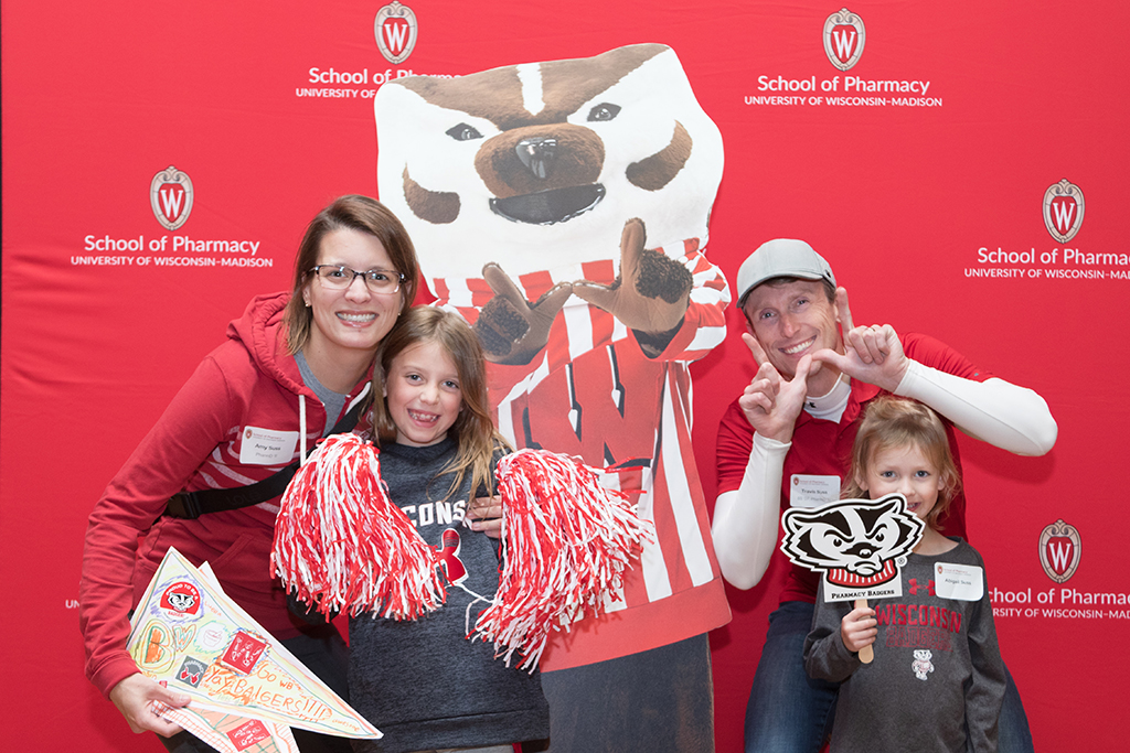 Alumnus with spouse and two young daughters posing with Bucky cardboard cutout