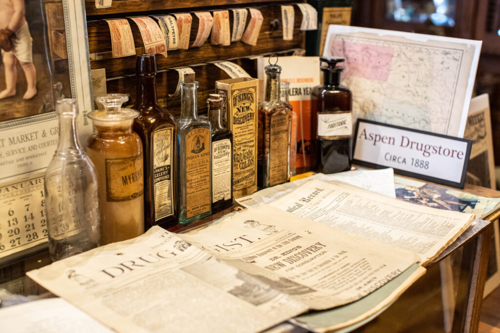 Aged glass bottles from Aspen Drugstore, circa 1888, and a Druggist newspaper.