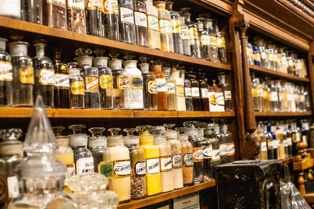 Long wooden shelves filled with glass pharmaceutical jars with gold-leafed labels.
