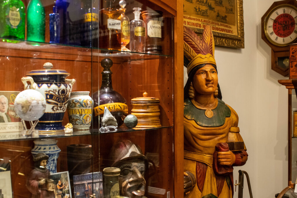 A glass case filled with ceramic and glass jars and a wooden carving of a native woman with a headdress on.