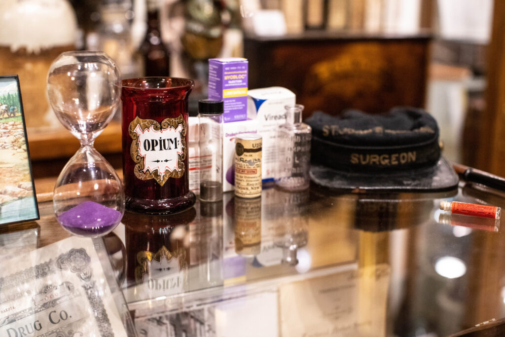 An old surgeon hat, a glass jar labeled "Opium," an hour glass with purple sad, and other assorted bottles.