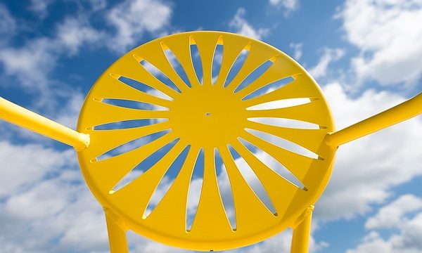 A yellow Memorial Union Terrace chair is pictured against a sunny blue sky at UW-Madison.. The chair is known for its iconic sunburst design. (Photo by Jeff Miller/UW-Madison)