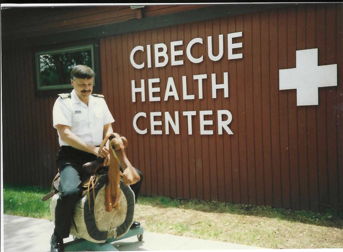 Captain Thomas Blumenberg (BS ’74) in his uniform on a rocking horse outside of Cibecue Health Center.